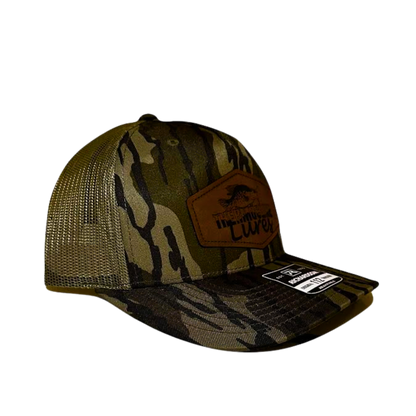 Opposite side profile of the Thermocline Lures Mossy Oak Bottomland camo trucker hat, showcasing its detailed leather patch logo and adjustable mesh back.