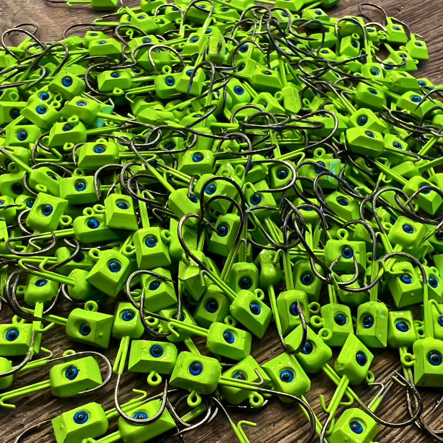 A large pile of bright green chartreuse Thermocline Hex Wedge Jig Heads with blue 3D eyes. The hexagonal design enhances sonar reflection, making them ideal for crappie and bass fishing.