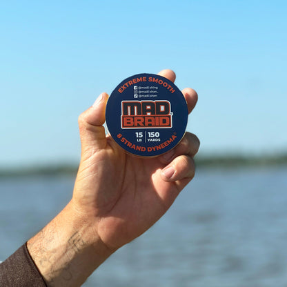 A fisherman holds a spool of Mad Braid braided fishing line against a clear blue sky, showcasing its extreme smoothness and strength for precision casting and durability.